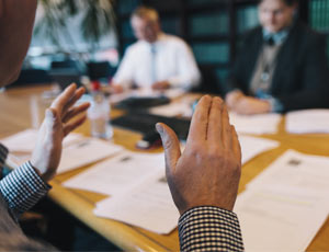 Three people having a discussion in a boardroom with various documents laid on on the table